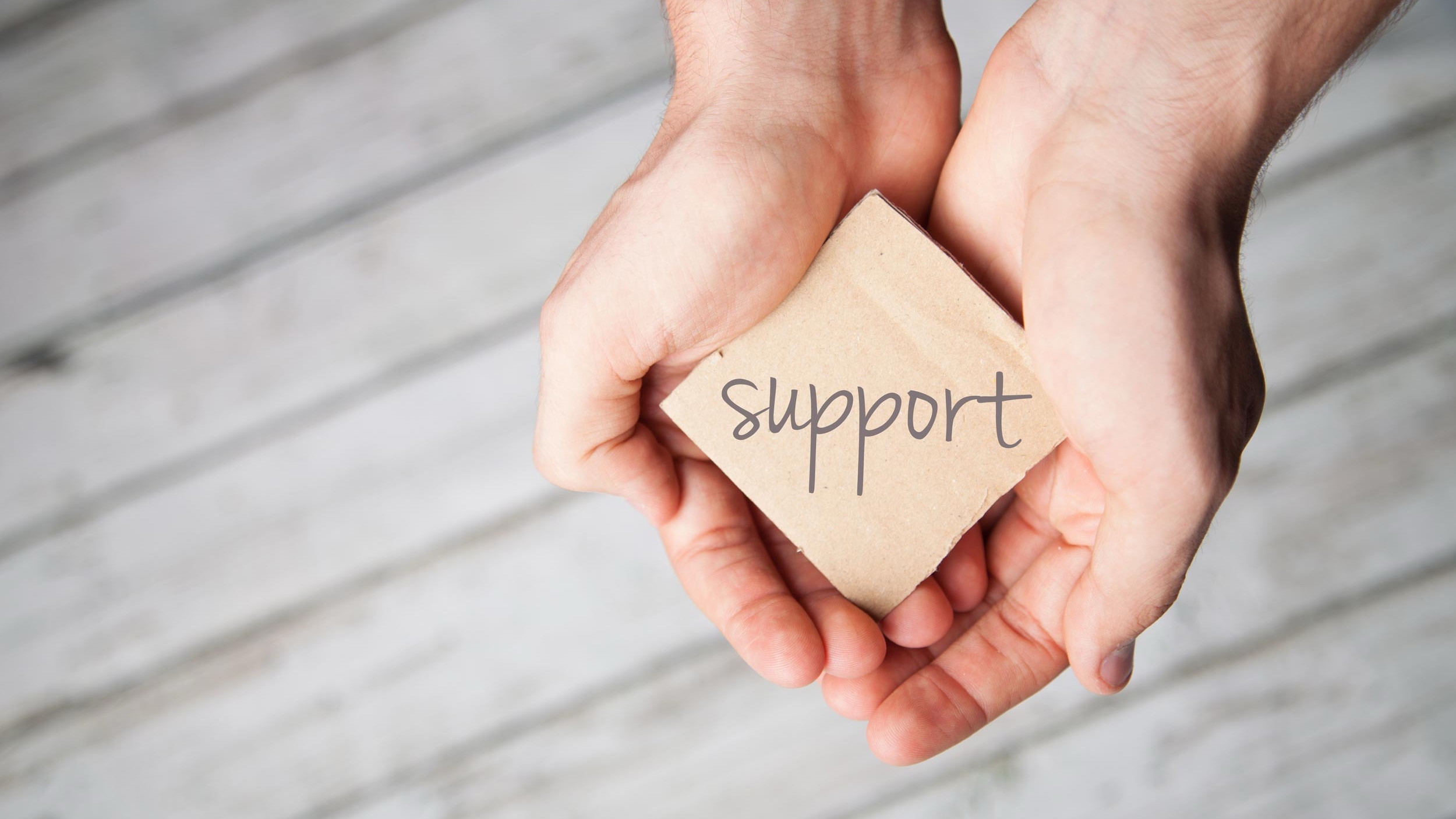 Two hands holding a piece of cardboard with the word "support" written on it