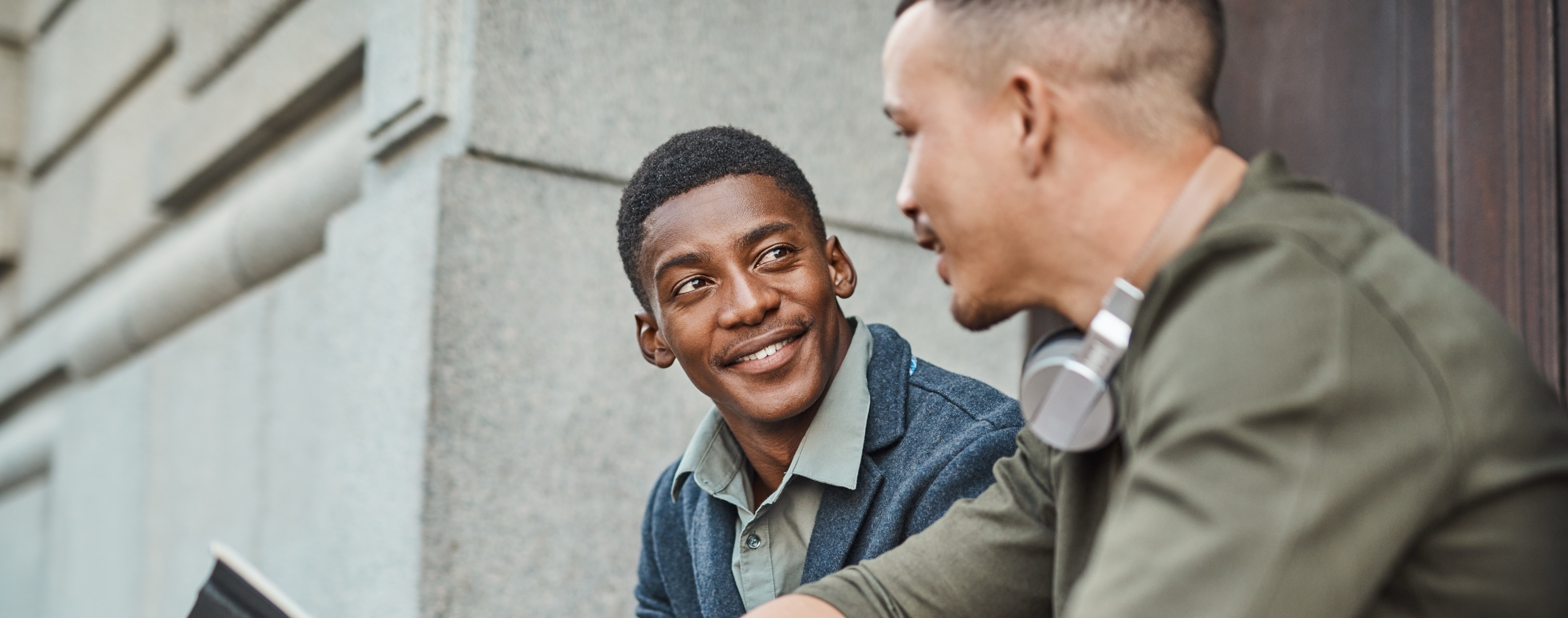Two men sitting on the steps outside, speaking to each other